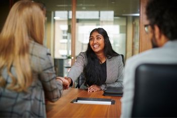 A woman in a job interview smiling and shaking the hand of the interviewer.